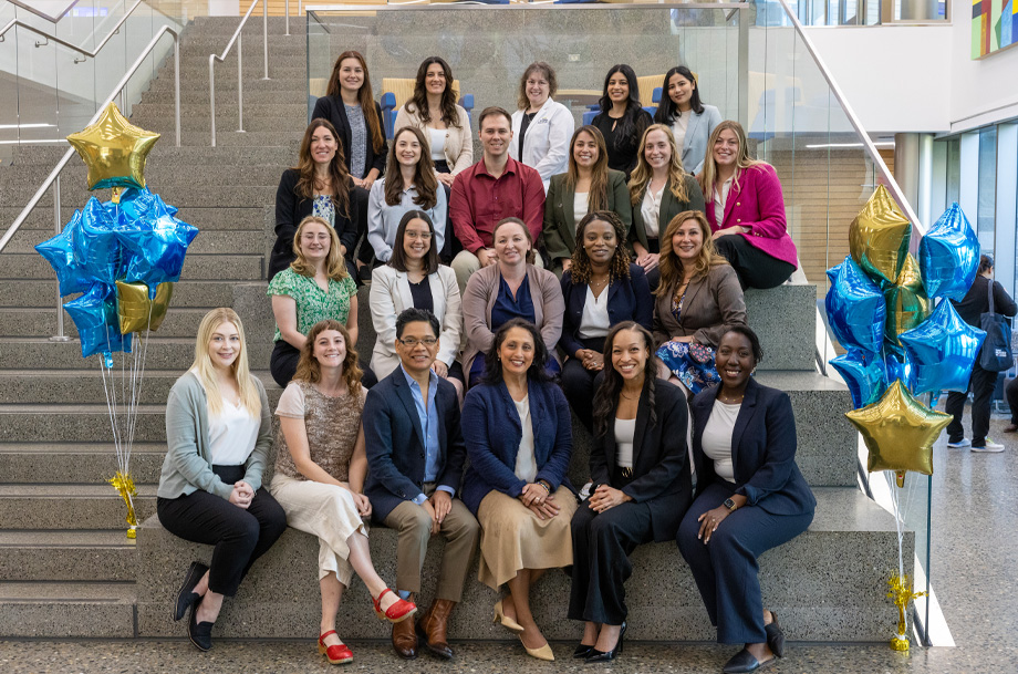 Students sit side-by-side on staircase and smile toward camera
