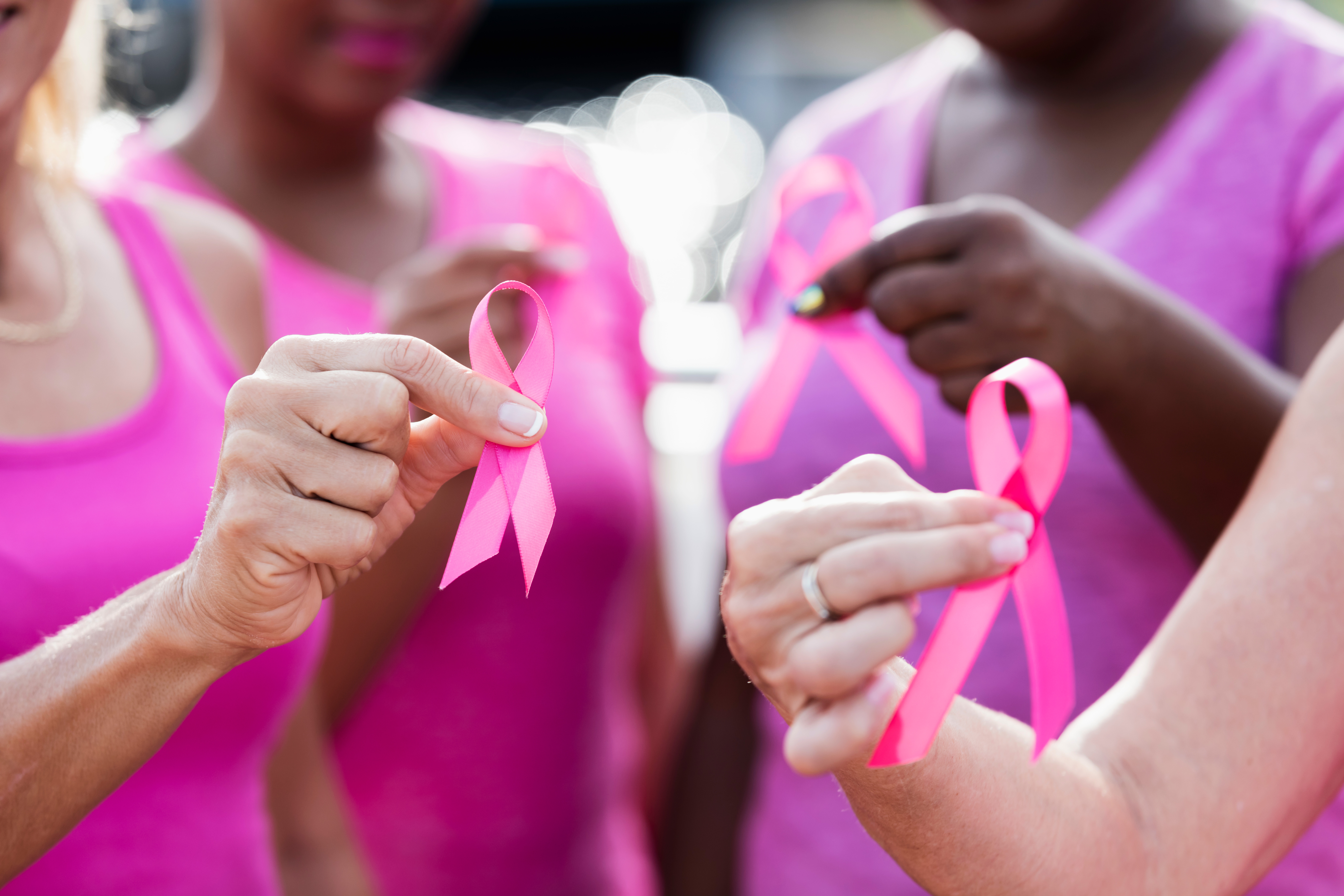 Group of four women with pink shirts holding pink breast cancer ribbons.