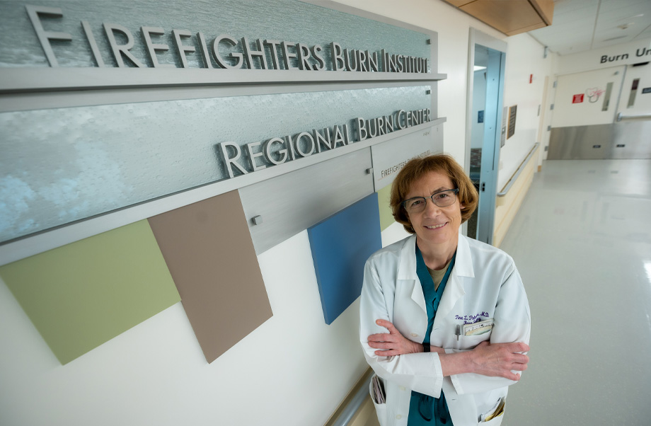  A woman wearing white doctor&rsquo;s coat next to wall sign that reads: Firefighters Burn Institute Regional Burn Center.