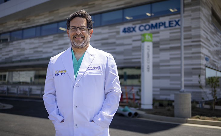 A doctor in a white coat stands outside UC Davis Health's 48X building
