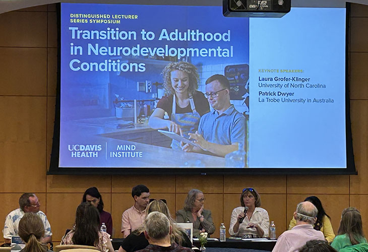 A panel of presenters sits in front of a crowd at the UC Davis MIND Institute auditorium