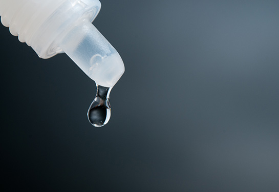 Dark gray background wih a drop coming out of a white bottle 