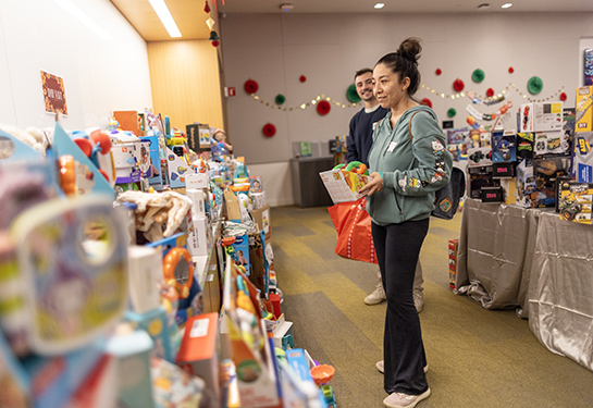 A person wearing a green hoodie is holding a small toy while viewing dozens of toys arranged on a countertop.