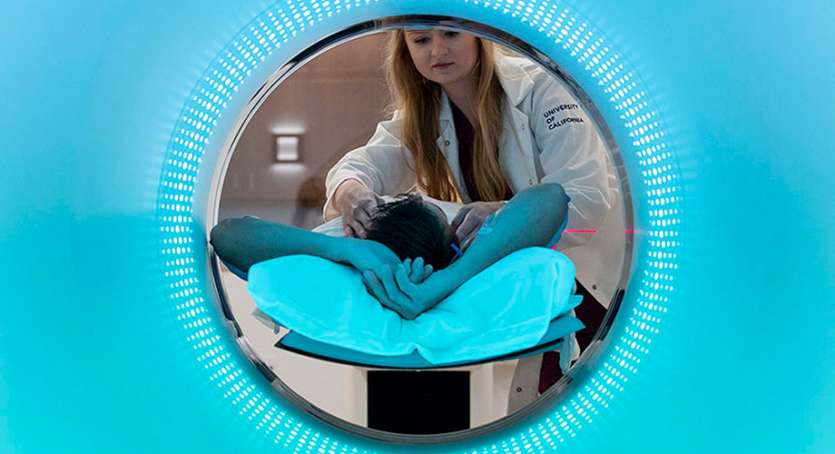 A patient is lying down on a full body scanner while a doctor helps them get situated. 