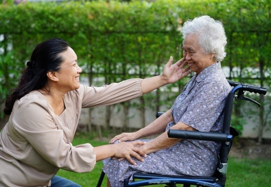 A caretaker smiles at a happy-looking elderly woman in a wheelchair