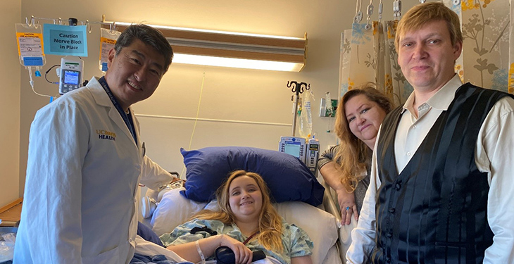 In the center, Tiffany Balts in a hospital bed after her surgery. Neurosurgeon Kee Kim standing to Tiffany&rsquo;s right and her mother and dad to her left.