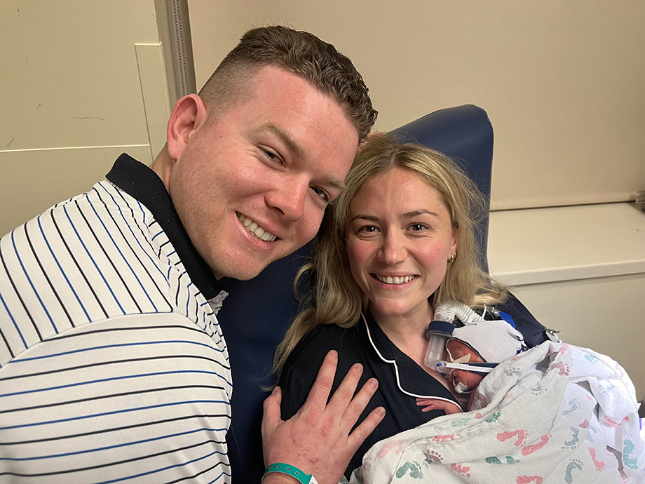 Man puts his hand on woman's shoulder as she holds newborn baby.
