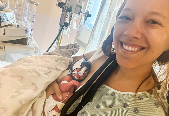 Side view of mother's head as she looks down at her premature baby she is holding in her arms.