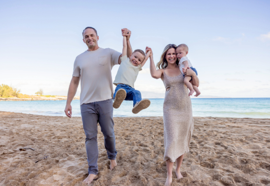 Man and woman standing on beach holding two boys in the air. 