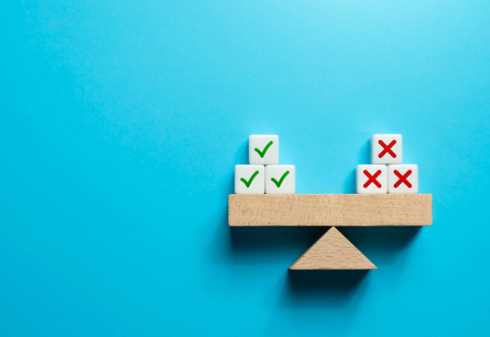 A model of a wooden teeter totter with three blocks with check marks on the left and three blocks with red x's on the right.
