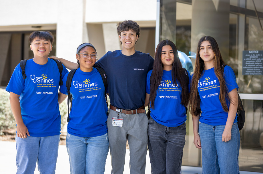 tudents in blue SHINES shirts stand on either side of program graduate Matthew Perez with arms interlocking