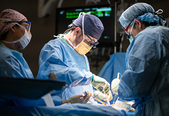 3 doctors in blue gowns, masks and caps in an operating room